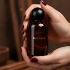 Hand holding a perfume bottle labeled 'Oud Amour' with a blurred background