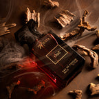 Perfume bottle labeled 'Noir - Oud' with smoke and wood pieces on a dark background