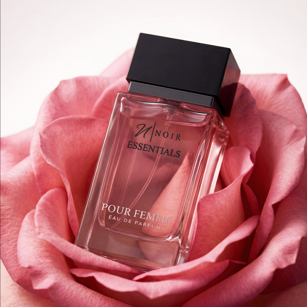 Perfume bottle labeled 'Noir Essentials Pour Femme' surrounded by pink roses on a light background