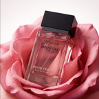 Perfume bottle labeled 'Noir Essentials Pour Femme' surrounded by pink roses on a light background