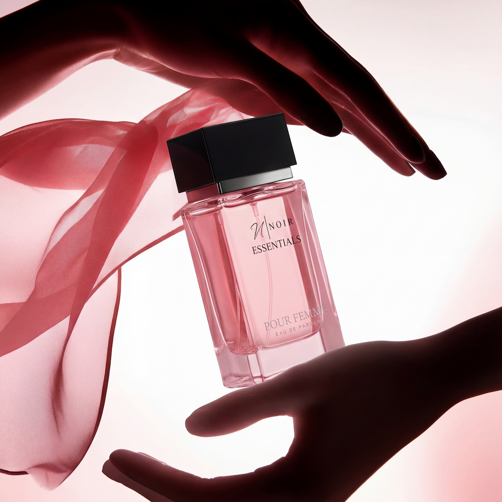 Perfume bottle held by two hands with a soft pink background