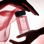 Perfume bottle held by two hands with a soft pink background