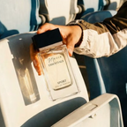 Person holding a perfume bottle labeled 'Essentials Sport' on an airplane seat