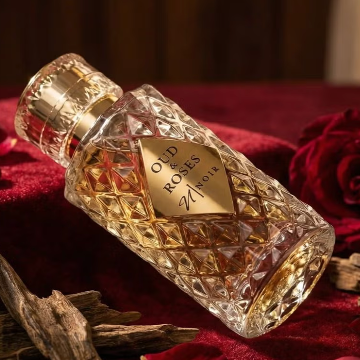 Perfume bottle labeled 'Oud Roses Noir' on a red fabric background with roses and wood elements.