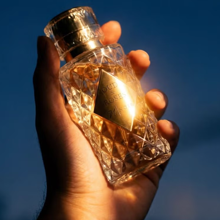 Hand holding a gold and crystal perfume bottle against a blue sky