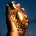 Hand holding a gold and crystal perfume bottle against a blue sky