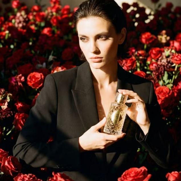 Woman holding a perfume bottle surrounded by red flowers